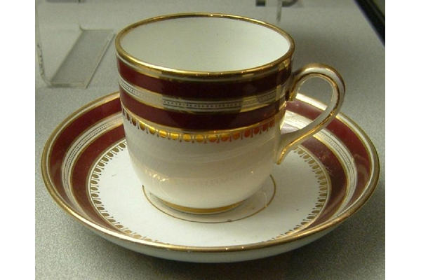 Late 19th century glazed ceramic cup and saucer manufactured by the Clyde Pottery, Greenock. Decorated in white with a decorated band on upper part, two rows of red interspersed with rows of gilding, also gilding above and below red, bottom row is lambrequin border of alternating line and circle. - L1977.131 - © McLean Museum and Art Gallery, Greenock.