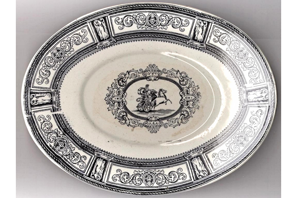 Late 19th century glazed ceramic plate for sauce boat manufactured by the Clyde Pottery Company, Greenock. Decorated with the 'Chariot' pattern of a charioteer, receding, with two prancing horses in central cartouche, heavily decorated with classical scrollwork; border, scrollwork, narrow reserves with female classical figures. Made between 1884 and 1900. - 1987.598 - © McLean Museum and Art Gallery, Greenock.