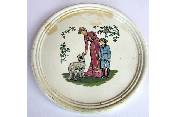 Late nineteenth century Clyde Pottery plaque decorated with a design of a woman standing patting a dog with boy standing next to her. Decorative foliage on either side. Made between 1862 and 1900 by the Clyde Pottery Company, Greenock. - 2011.100 - © McLean Museum and Art Gallery, Greenock.