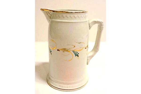 Jug manufactured by the Clyde Pottery, Greenock with almost straight sides with curving inward near top. Decorated with a white, zigzag pattern in relief round upper edge; gilt band around rim and foot, gold and green foliage in band around middle of jug is moulded. Made around 1877. - L1977.140 - © McLean Museum and Art Gallery, Greenock.