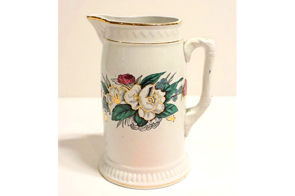 Jug manufactured by the Clyde Pottery Company, Greenock. Decorated with the 'York' pattern. White background with zigzag pattern in relief around rim; narrow gilt band round rim and foot. Band of decoration around middle, floral pattern in green, pink, turquoise and gold. Mark on back 'YORK C.P.Co' inside laurel branches and surmounted by crown. - L1977.142 - © McLean Museum and Art Gallery, Greenock.
