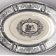 Late 19th century glazed ceramic plate for sauce boat manufactured by the Clyde Pottery Company, Greenock. Decorated with the 'Chariot' pattern of a charioteer, receding, with two prancing horses in central cartouche, heavily decorated with classical scrollwork; border, scrollwork, narrow reserves with female classical figures. Made between 1884 and 1900. - 1987.598 - © McLean Museum and Art Gallery, Greenock.