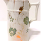 Glazed ceramic jug manufactured by the Clyde Pottery Company, Greenock. Decorated with a hand painted design, a white background and a design of green flowers and gilded strips. - 1980.108 - © McLean Museum and Art Gallery, Greenock.