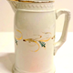 Jug manufactured by the Clyde Pottery, Greenock with  almost straight sides with curving inward near top. Decorated with a white, zigzag pattern in relief round upper edge; gilt band around rim and foot, gold and green foliage in band around middle of jug is moulded. Made around 1877. - L1977.140 - © McLean Museum and Art Gallery, Greenock.